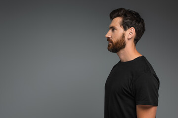 side view of bearded man in black t-shirt looking away isolated on grey.
