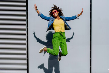 Young happy multiracial teenage girl with sunglasses and afro hairstyle, jumping and posing outdoor.