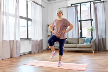 sport, fitness and healthy lifestyle concept - smiling senior woman exercising on mat at home