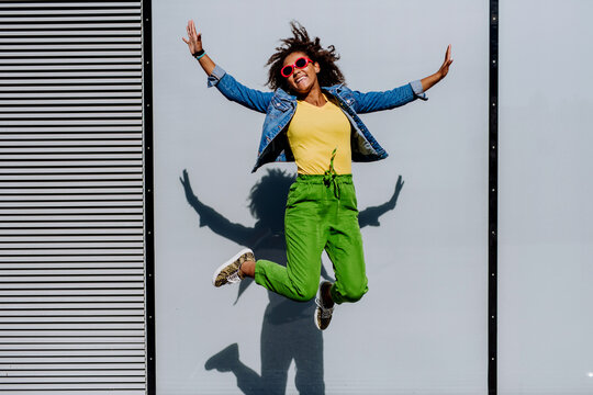 Young happy multiracial teenage girl with sunglasses and afro hairstyle, jumping and posing outdoor.