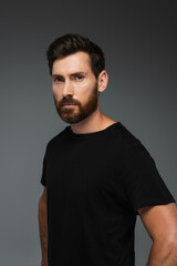 portrait of bearded man in black t-shirt looking at camera isolated on grey.