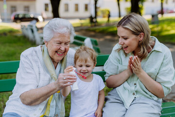 Happy smiling woman with senior grandmother and little daughter blowing soap bubbles at park,...