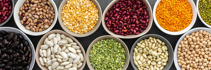 Banner of different types of legumes in bowls, yellow and green peas, mung beans and chickpeas , colored beans and lentils, top view, copy space