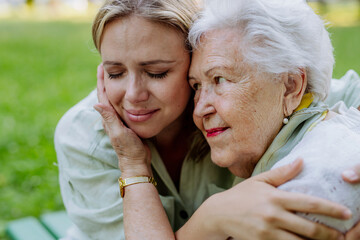 Worried senior grandmother comforting grown up granddaughter when sitting on bench in park, share problem with someone close concept