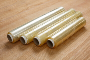 Close up on wooden table lies four rolls of transparent food film on cardboard spool.