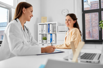 medicine, healthcare and people concept - female doctor with clipboard talking to smiling woman...