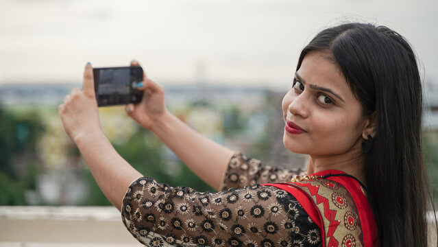 Beautiful Indian woman taking photo with her mobile phone camera, young female Asian photographer