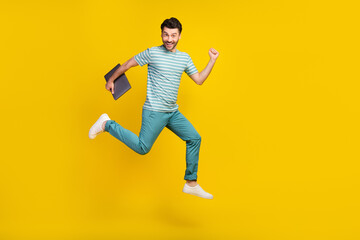 Fototapeta na wymiar Full length photo of ecstatic handsome man wear striped t-shirt blue pants hold laptop run on vacation isolated on yellow color background