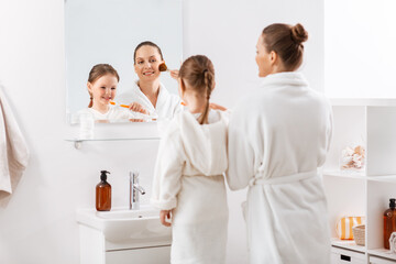 beauty, family and people concept - happy smiling mother applying make up and little daughter brushing teeth in bathroom