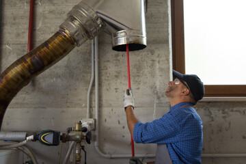 Picture of a handyman cleaning the stainless steel pipe of a boiler flue with a brush. I work as a...