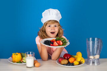 Child chef dressed cook baker apron and chef hat hold plate with fruits isolated on studio background. Healthy nutrition kids food.