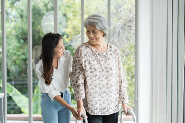 Young woman help elderly woman walk with walker careful at hospital. Woman caring senior woman at nursing home. - obrazy, fototapety, plakaty