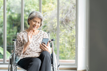 Elderly asian woman using mobile phone on wheelchair. Asian senior grandma use smart phone while...