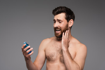 Fototapeta premium bearded and shirtless man holding bottle with after shave product isolated on grey.