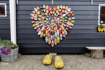 Zapatos de madera adornados con diferentes motivos colgados en una pared formando un corazón....