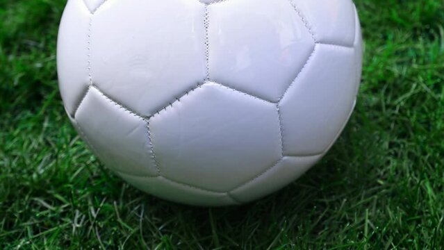 A close up camera rotating around a white football soccer ball on a green grass field.