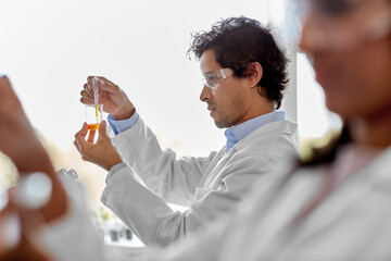 science research, work and people concept - male scientist with chemical or test sample in beaker and dropper working in laboratory