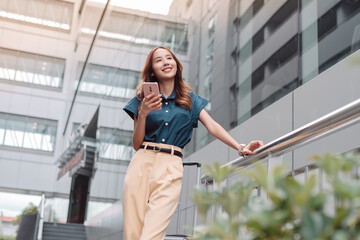 Beautiful asian female businesswoman use smartphone, Walk enjoy smiling while doing commuting in the modern city near office building outside