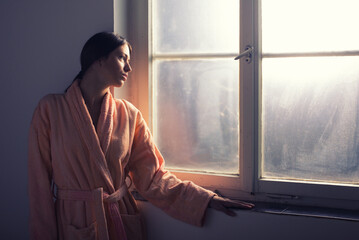 Woman cancer patient in bathrobe standing in front of the hospital window
