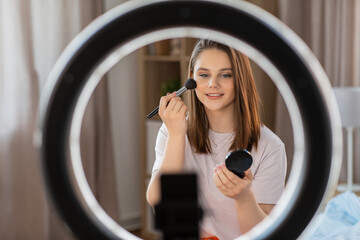 beauty blogging, technology and people concept - happy smiling girl blogger with ring light and smartphone applying make up at home