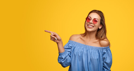Happy young lady pointing away and smiling in yellow studio