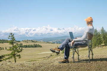 Mature man traveler uses laptop computer on mountain top,  enjoying nature landscape view outdoors. work remote concept.