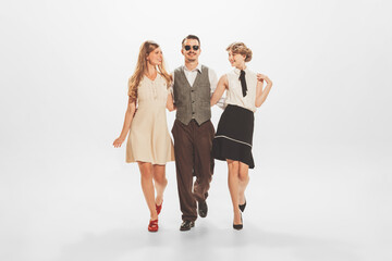 Fototapeta premium Portrait of stylish people in vintage clothes, man walking with two beautiful women, posing isolated on white background