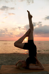Fototapeta na wymiar fitness, sport, and healthy lifestyle concept - woman doing yoga shoulderstand on beach over sunset
