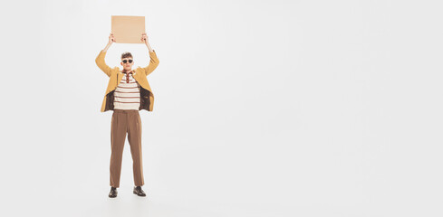 Portrait of young man in yellow jacket standing with cardboard sign, poster above head isolated over white studio background