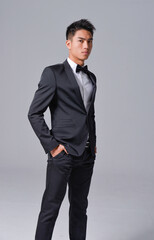 Handsome fashion model.
elegant man wear formal black suit with bow tie on gray background 

