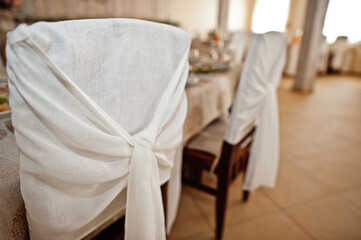 Fototapeta na wymiar Chairs with white ribbons at wedding table in restaurant.