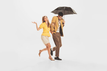 Portrait of young stylish couple, man and woman walking under umbrella isolated over white studio background