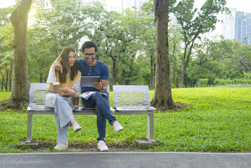 happy asian people using  tablet to work, romantic young couple sitting on bench and chatting in...