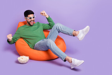 Full body photo of young latin man sit soft beanbag raise fists enjoy movie dressed stylish green...