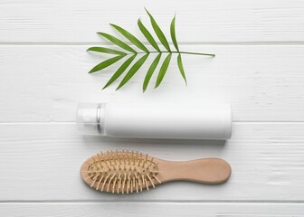 Dry shampoo spray, hairbrush and green twig on white wooden table, flat lay