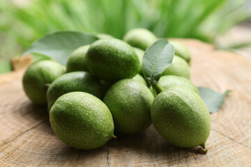 Many green walnuts and leaves on wooden stump against blurred background, closeup