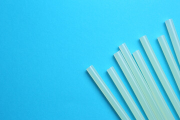 Many glue sticks on light blue background, flat lay. Space for text
