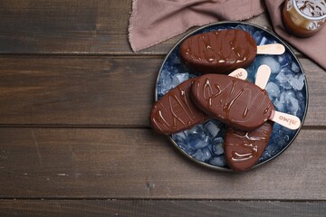 Delicious glazed ice cream bars and ice cubes on wooden table, flat lay. Space for text