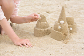 Fototapeta na wymiar Child decorating sand castle with shell on beach, closeup