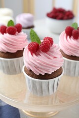 Delicious cupcakes with cream and raspberries on stand