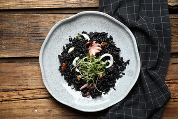 Delicious black risotto with seafood on wooden table, top view