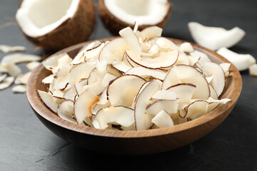 Tasty coconut chips in bowl on black table