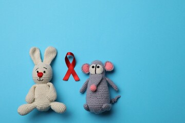 Cute knitted toys and red ribbon on blue background, flat lay with space for text. AIDS disease awareness