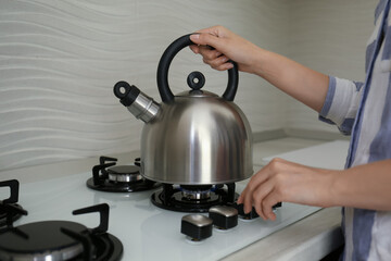 Woman putting kettle on gas stove in kitchen, closeup