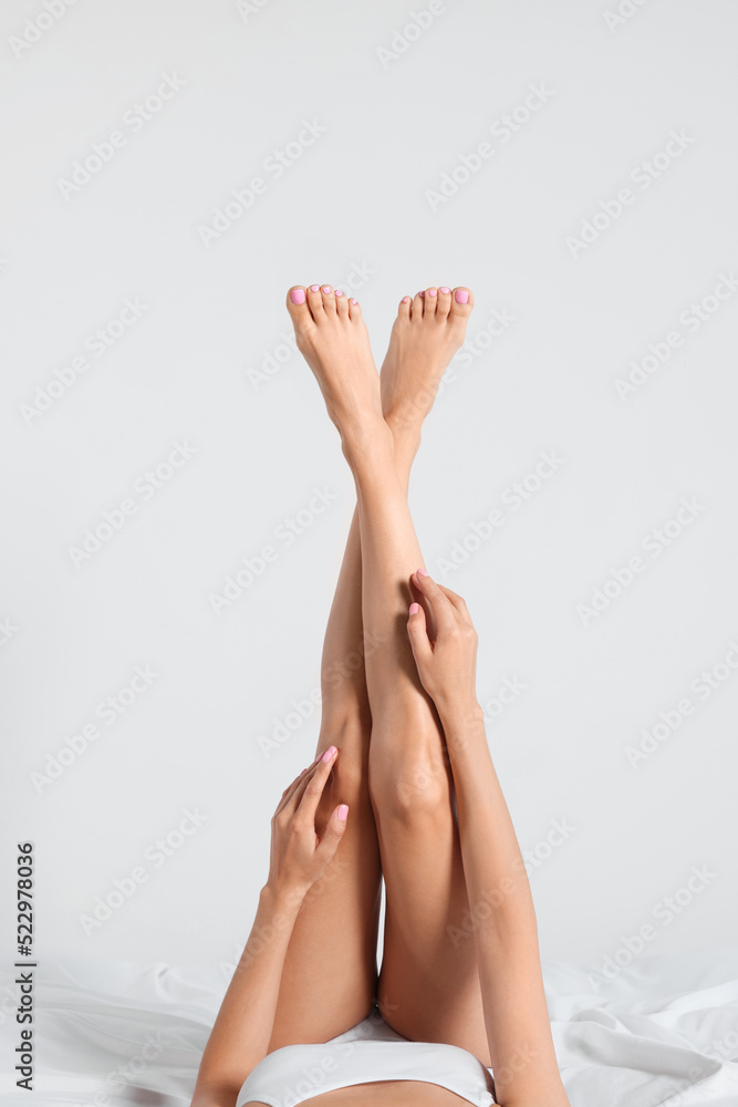 Poster Woman with beautiful smooth legs on bed against white background, closeup