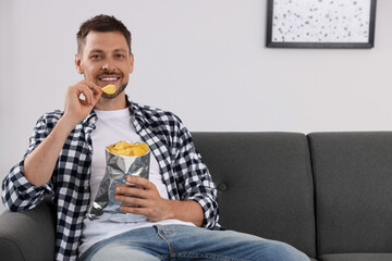 Handsome man eating potato chips on sofa at home