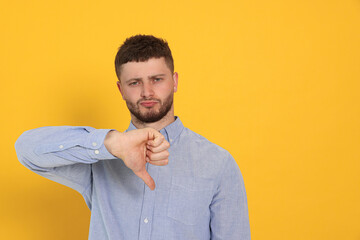 Young man showing thumb down on orange background, space for text