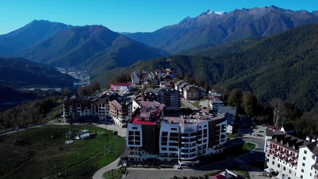 Rosa khutor village surrounded majestic caucasian mountain ridge. deep wooded slopes and mountain peaks covered with snow in the sky with no clouds on sunny fall day.