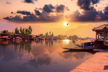 Fototapeta na wymiar Beautiful scenic view colorful sunset above calm water of Dal Lake with dramatic cloudy sky and traditional boat (shikara) shadow figures, Srinagar, Jammu and Kashmir, Northern India, Central Asia.