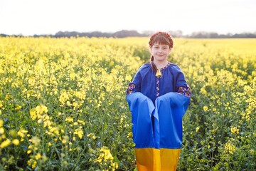 Pray for Ukraine. Child with Ukrainian flag in rapeseed field. Girl holding national flag in her hand.